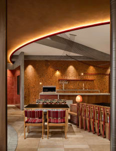 Warm and inviting kitchen and dining area with wooden floors and walls, featuring a dining table and chairs, couches, and decorative bottles