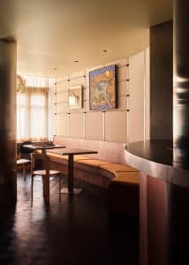 Wooden floors and walls in a restaurant with two dining tables, chairs, a couch, and a painting, creating an inviting atmosphere for socializing