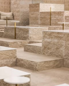 A modern and minimalistic indoor space with stone flooring, featuring steps leading to different levels and couches placed throughout