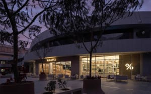 A modern building exterior at night with a white structure, multiple windows, and potted plants, accompanied by outdoor seating and a calm atmosphere