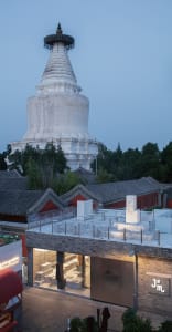 A red building with two towers, one larger than the other, set against a white structure in a warm sunset ambiance