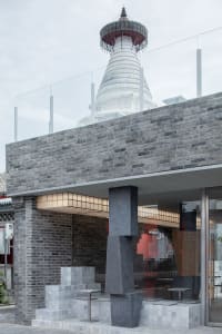 A brick building with a stone column and two benches, creating a calm and inviting atmosphere