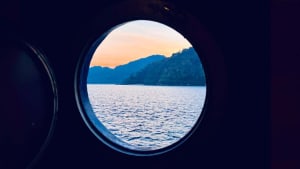 Calm ocean view through a round window on a boat, with the cabin visible in the background