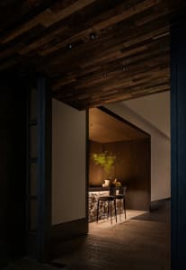 Warm and inviting kitchen space with wooden floors and walls, featuring a counter with two chairs and a potted plant