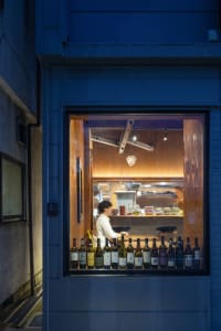 A cozy restaurant interior with a glass door, bottles on the counter, and a person standing nearby