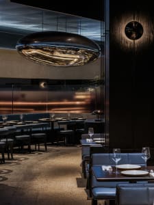 Dimly lit restaurant with black tables and chairs, wine glasses on some tables