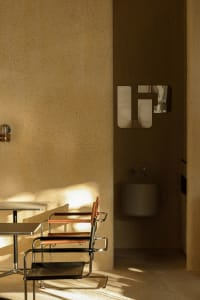 Modern bathroom with a white toilet, sink, and mirror, set against a concrete backdrop with two minimalist chairs