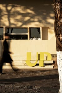 Outdoor cafe with a modern design, featuring a white building with a brick wall, chairs, and dining tables, set amidst a lively atmosphere