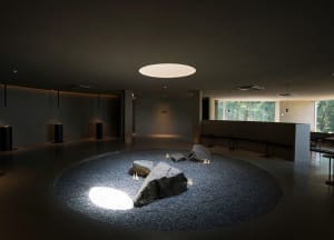 A serene indoor space with a large rock surrounded by smaller rocks and two benches, creating a calm atmosphere