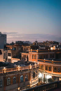 A bustling cityscape at night with tall buildings, arches, domes, and multiple windows, illuminated by lights and casting shadows