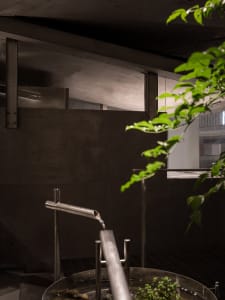 A modern bathroom with two sinks, one with running water, set against a concrete backdrop, creating a functional and minimalist atmosphere