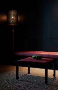 Darkened living space with a red bench, a bowl of green vegetables, and a cozy atmosphere