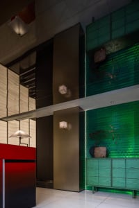 A modern interior space with a red wall, green tiles, glass dividers, and lush plants creating a lively atmosphere