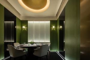 A dining area with a round table, four chairs, and various table settings in a modern restaurant with green walls and good lighting