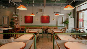 A modern Asian restaurant with a long dining table and multiple chairs, surrounded by tables with green accents on the walls and floors, creating an inviting and comfortable atmosphere