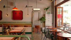 Dining area with multiple tables, chairs, and potted plants, surrounded by modern tiled walls