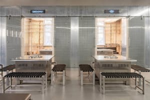 A modern kitchen and dining area with two dining tables, stainless steel walls, chairs, and well-lit space