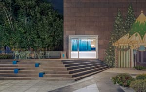 A modern building with a large window and concrete exterior, featuring two chairs outside in a nighttime setting