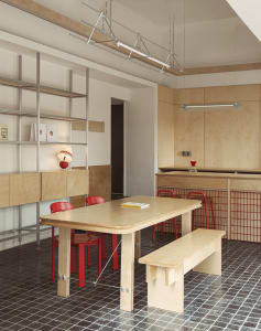 A warm and inviting kitchen and dining area with a wooden table, two red chairs, a smaller dining table, a sink, and a refrigerator, surrounded by books and exuding a cozy atmosphere