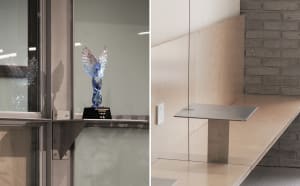 A modern office space with a glass wall and staircase, featuring a reflective surface and a trophy on display, with a clean and organized atmosphere