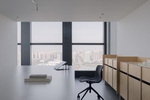 A modern office space with a large window offering a city view, featuring a desk, chairs, and a laptop, with a cup nearby, in a well-lit and comfortable atmosphere