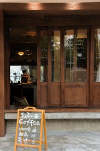 A cozy coffee shop with wooden walls, a window display, and comfortable seating areas, featuring a dining table and couch, with cups and bowls scattered throughout the scene