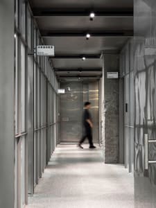 A modern hotel lobby with a silver metal finish, featuring two individuals walking down the hallway