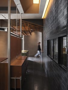 Casual dining space with a wooden table and chairs, a person walking towards the area and another person standing near the table