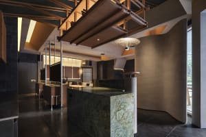 A restaurant dining area with tables, chairs, potted plants, wood, and stone walls, and various lighting fixtures