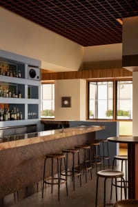 A bar area in a restaurant with a marble countertop, wooden stools, and bottles displayed, creating an elegant and inviting atmosphere