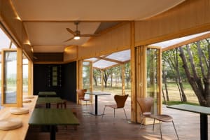 Modern restaurant interior with wooden floors and walls, featuring dining tables and chairs in a warm and inviting atmosphere