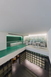 A modern restaurant with a glass ceiling, white walls, and green accents, featuring multiple dining tables and chairs