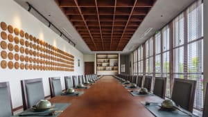 Spacious dining hall with a long wooden table and numerous chairs, set up for a formal event with several bowls on the table