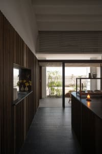 Open kitchen space with wooden floors and walls, featuring potted plants, vases, and a chair, with natural light and a cozy atmosphere
