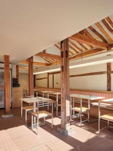 Rustic restaurant with wooden floors and walls, featuring dining tables, benches, and comfortable seating for guests