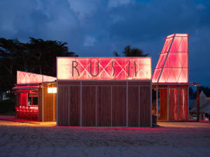 Two buildings on a beach with a pink-roofed structure and a wooden building, both with red lettering, in a relaxing and inviting environment
