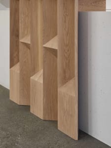 Three wooden bookshelves of varying heights against a white wall, creating a calm and organized atmosphere with neatly arranged books