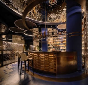 A social bar area with a circular counter, chairs, and a variety of bottles on display