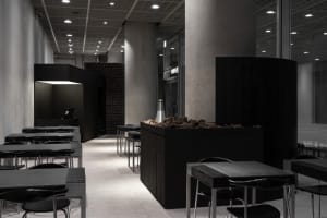 A bustling restaurant interior with brick and concrete walls, multiple dining tables, and chairs, featuring a mix of natural and artificial lighting
