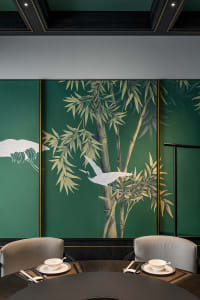 Serene living space with green walls, artwork of birds on bamboo trees, and two chairs in a calming environment