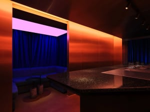 Modern bar area with a pink accent wall, black countertop, and a dining table, featuring two couches and three chairs
