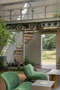 A comfortable living area with a green couch, two potted plants, and fans on the wall, creating a relaxing atmosphere