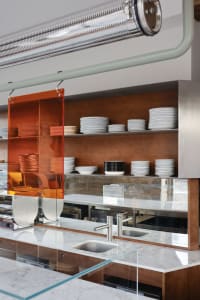 A modern kitchen with a dining table, sink, and plates on display, featuring marble countertops and a clean, well-lit atmosphere