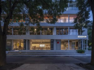 A modern building with a glass exterior, featuring many windows and a sophisticated entrance with seating for guests