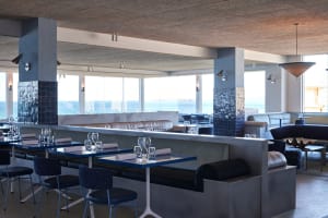 A modern restaurant interior with a large dining area featuring wooden tables and chairs, wine glasses, and an inviting atmosphere