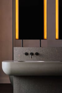 A bathroom with two sinks, marble countertops, and an orange glow creating a warm atmosphere