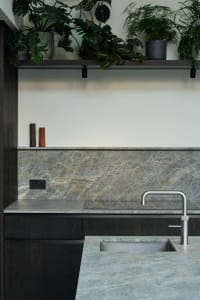 A bright and inviting kitchen with a marble countertop, sink, and cabinets, surrounded by potted plants and natural light