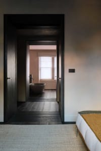 Bathroom with wooden floors and walls, featuring a freestanding bathtub surrounded by wooden panels and natural light from two windows