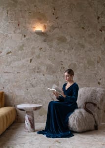 A woman sits on a chair in a cozy living area with a couch, dining table, and two chairs, surrounded by warm and inviting decor
