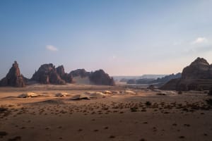 A desert landscape with mountains in the background, featuring several tents of varying sizes and positions, creating a sense of depth and adventure
